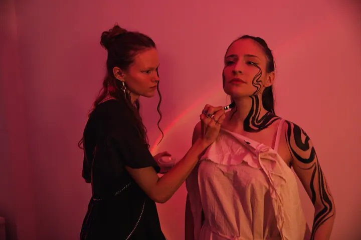 Artist painting flowing black lines on a model’s neck and face