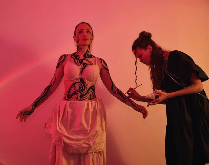 Artist painting flowing black forms on a model’s body