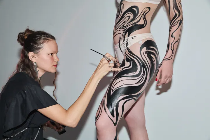 Artist painting flowing black forms on a model’s body