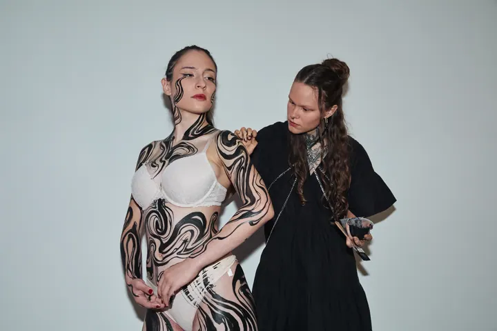Artist painting flowing black forms on a model’s body