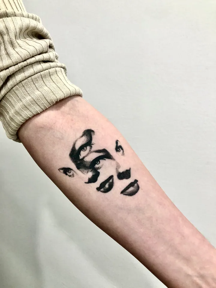 Surreal tattoo of eyes and lips on the forearm
