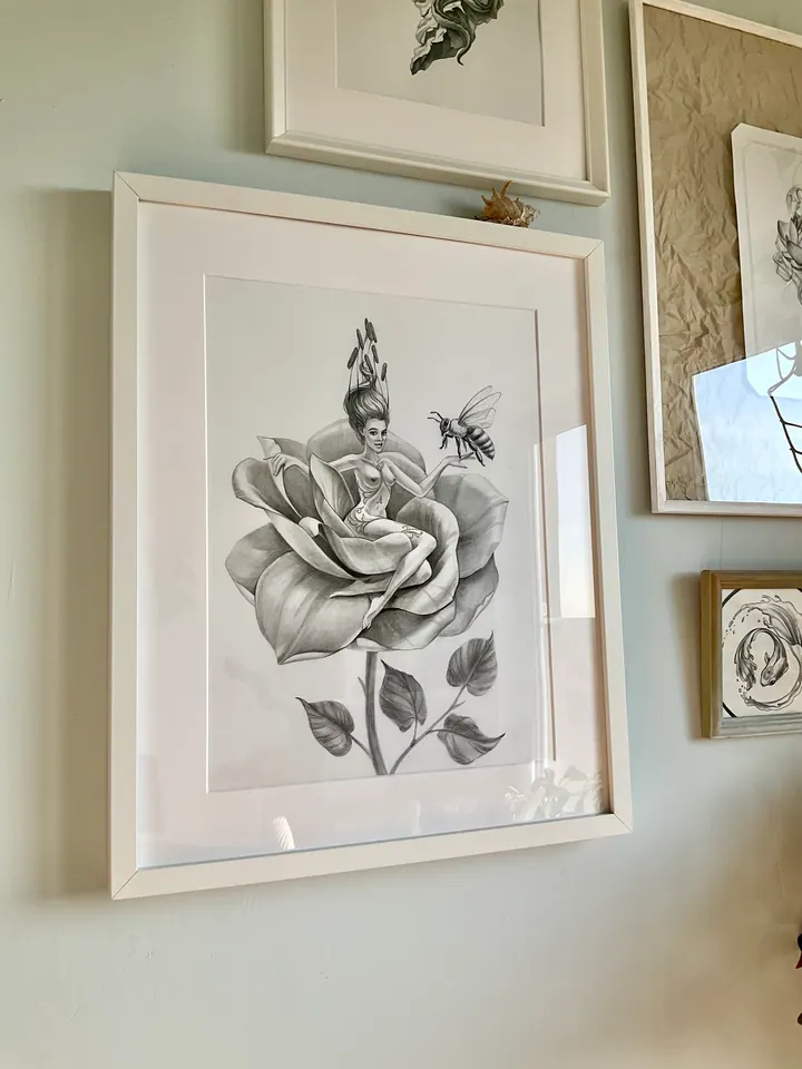 Framed drawing of a figure on a rose with a bee