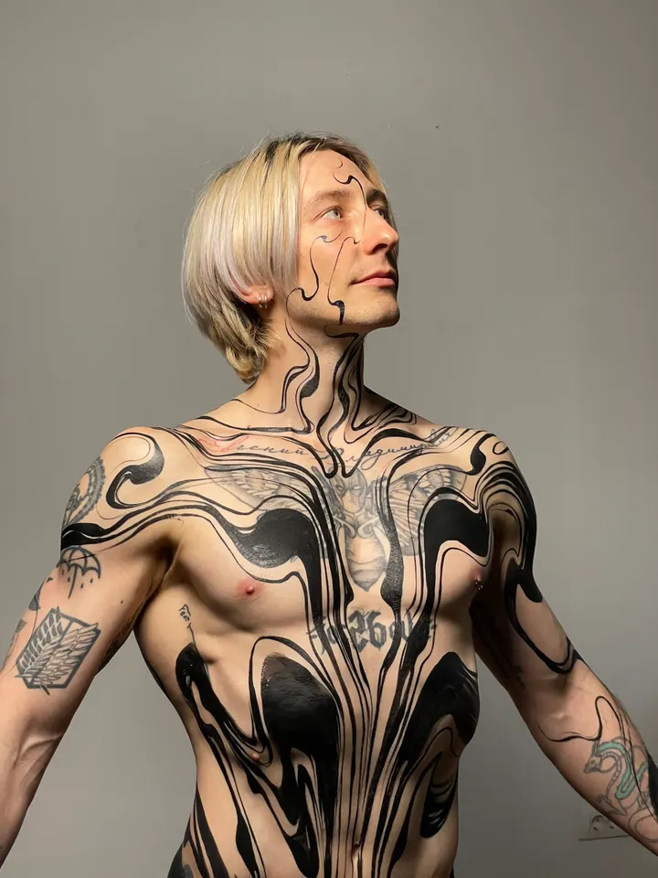 Flowing black body painting across a tattooed model’s torso