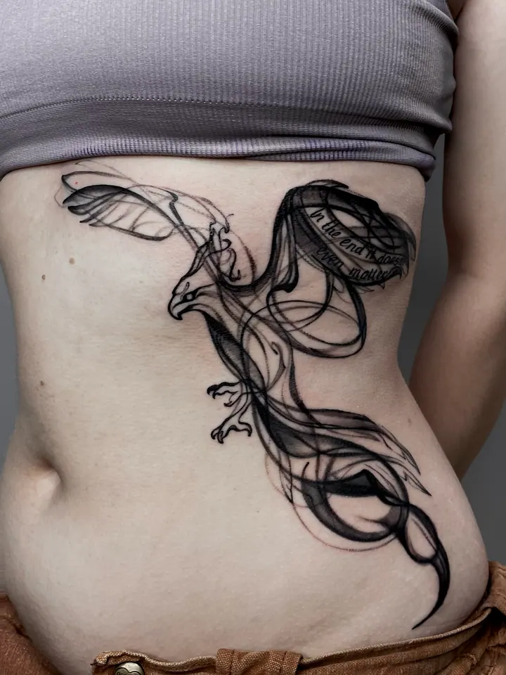 Bird tattoo with flowing wings and lettering on the ribs