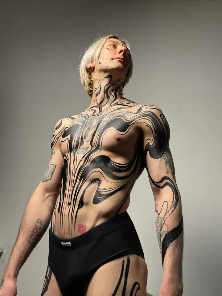 Flowing black body painting across a tattooed model’s torso