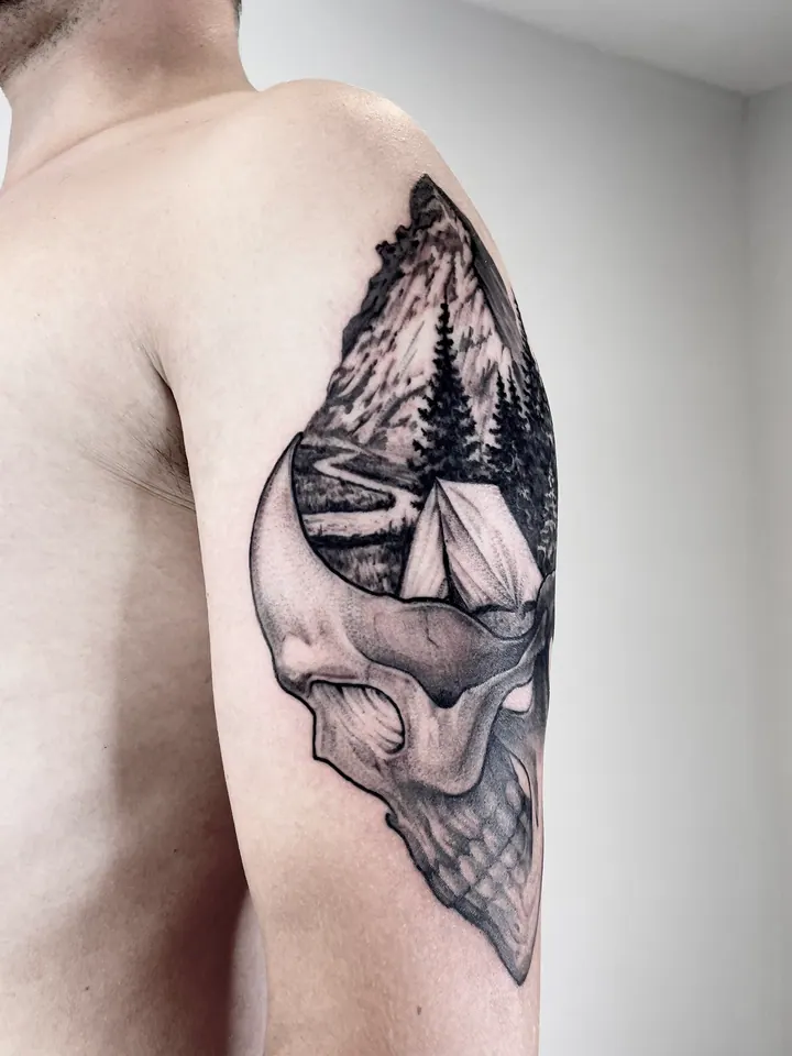Skull tattoo with a mountain, forest and tent on the upper arm