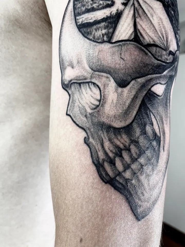 Skull tattoo with a mountain, forest and tent on the upper arm